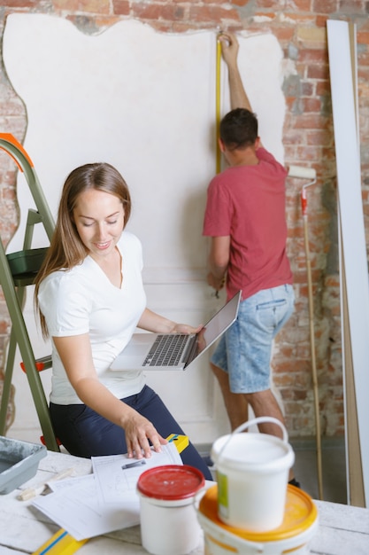 young-couple-doing-apartment-repair-together-themselves-married-man-woman-doing-home-makeover-renovation-concept-relations-family-love-measuring-wall-before-painting-design-making_155003-23102